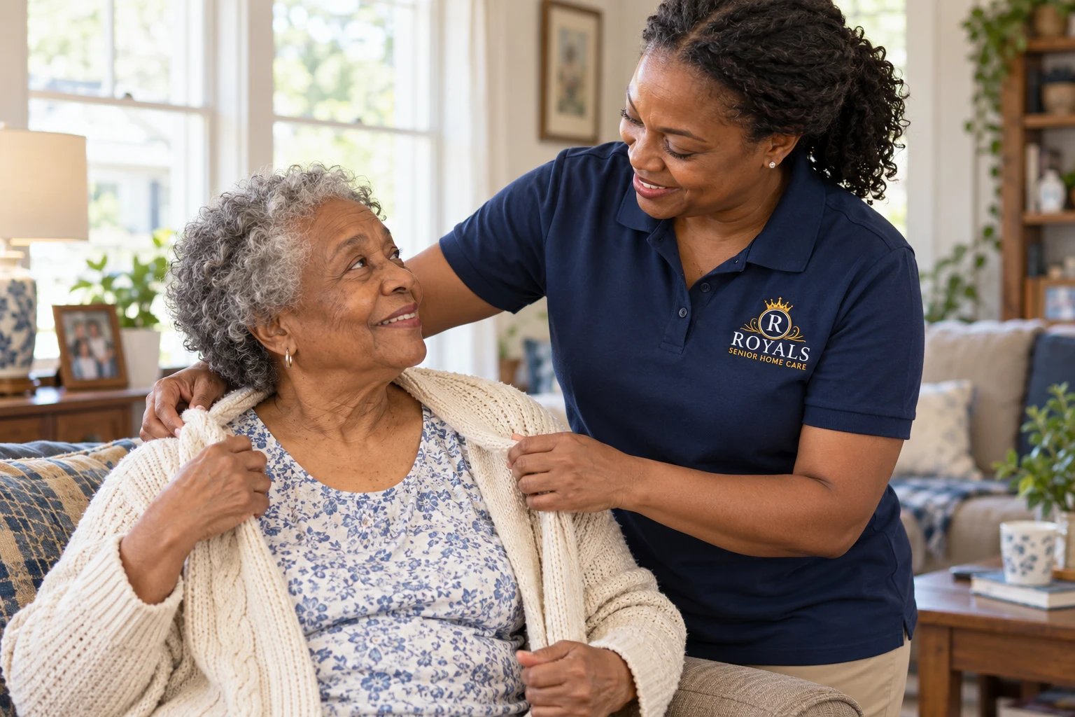 a caregiver in a Royals-branded polo helping an older adult with a cardigan